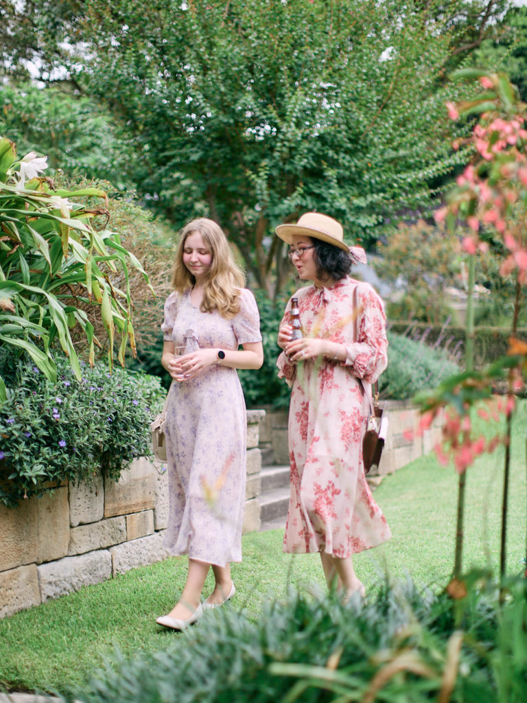 2 ladies holding drinks walking through garden talking