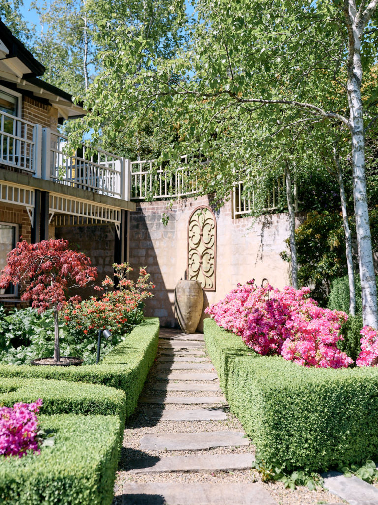 Path through garden surrounded by green hedges and pink flowers at Echoes Boutique Hotel wedding