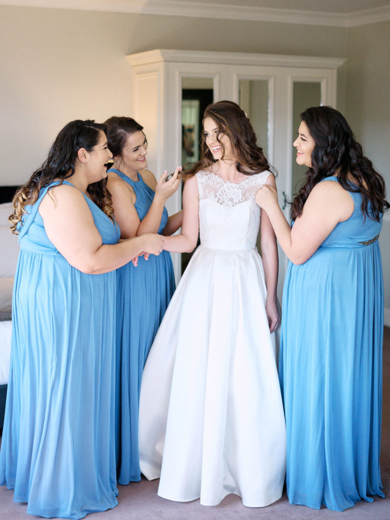 Bridesmaids in blue dresses laughing with bride in her wedding dress