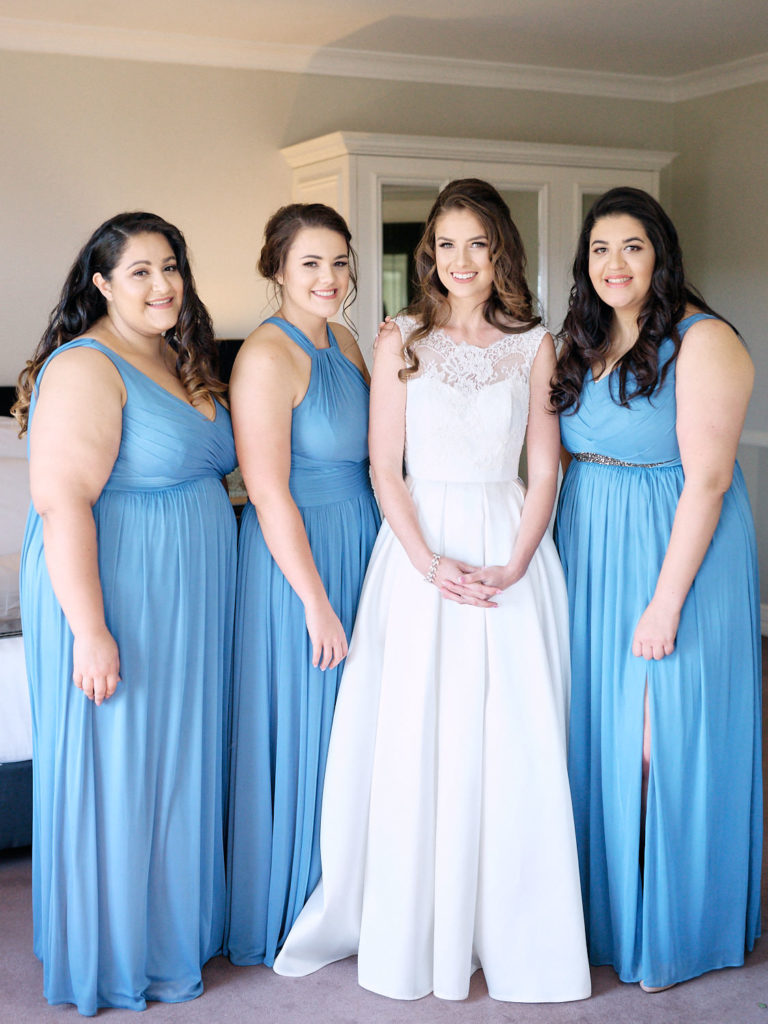 Bride in her wedding dress with bridesmaids in blue dresses smiling at the camera