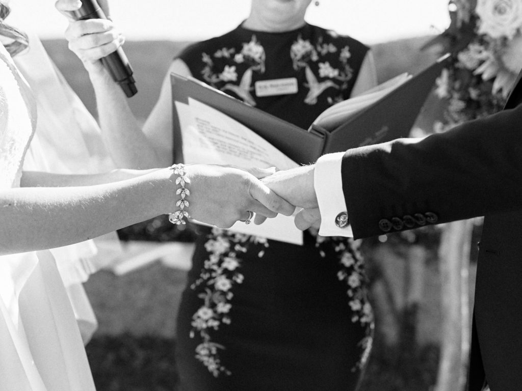 Black and white closeup of bride and groon holding hands during wedding ceremony