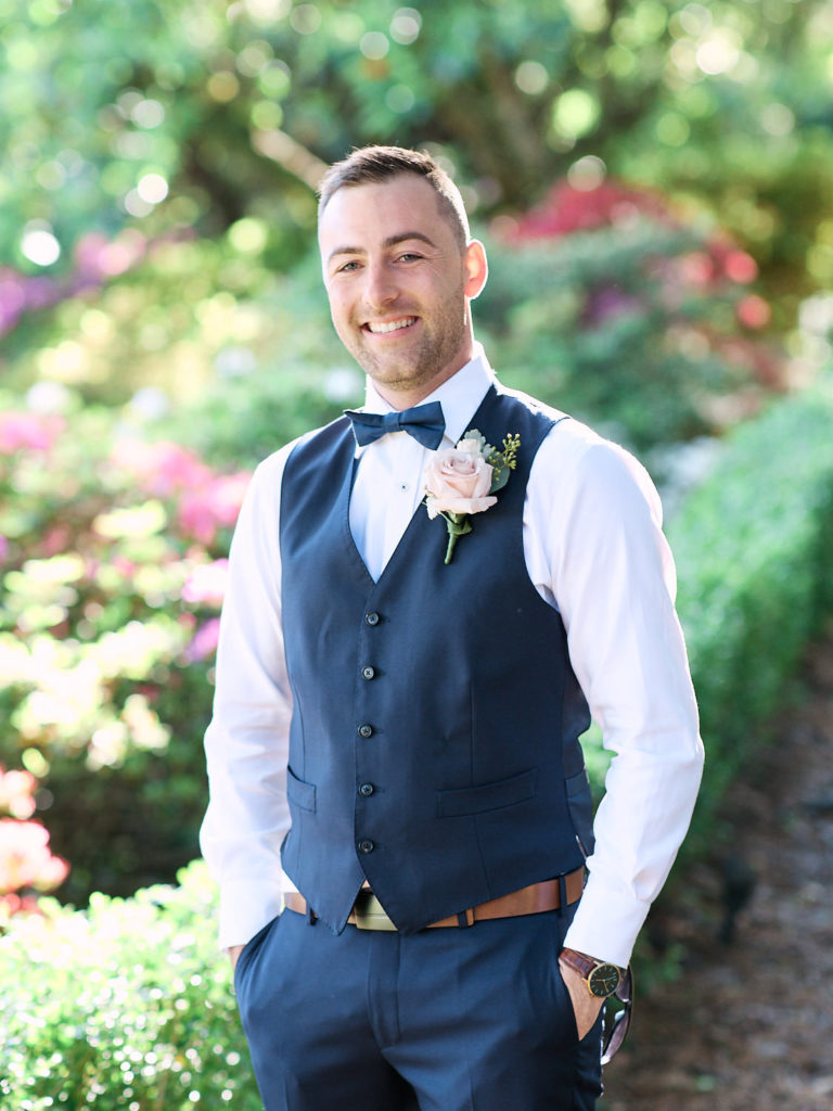 Groomsman wearing blue vest and boutonniere in gardens at Echoes Boutique Hotel and Restaurant