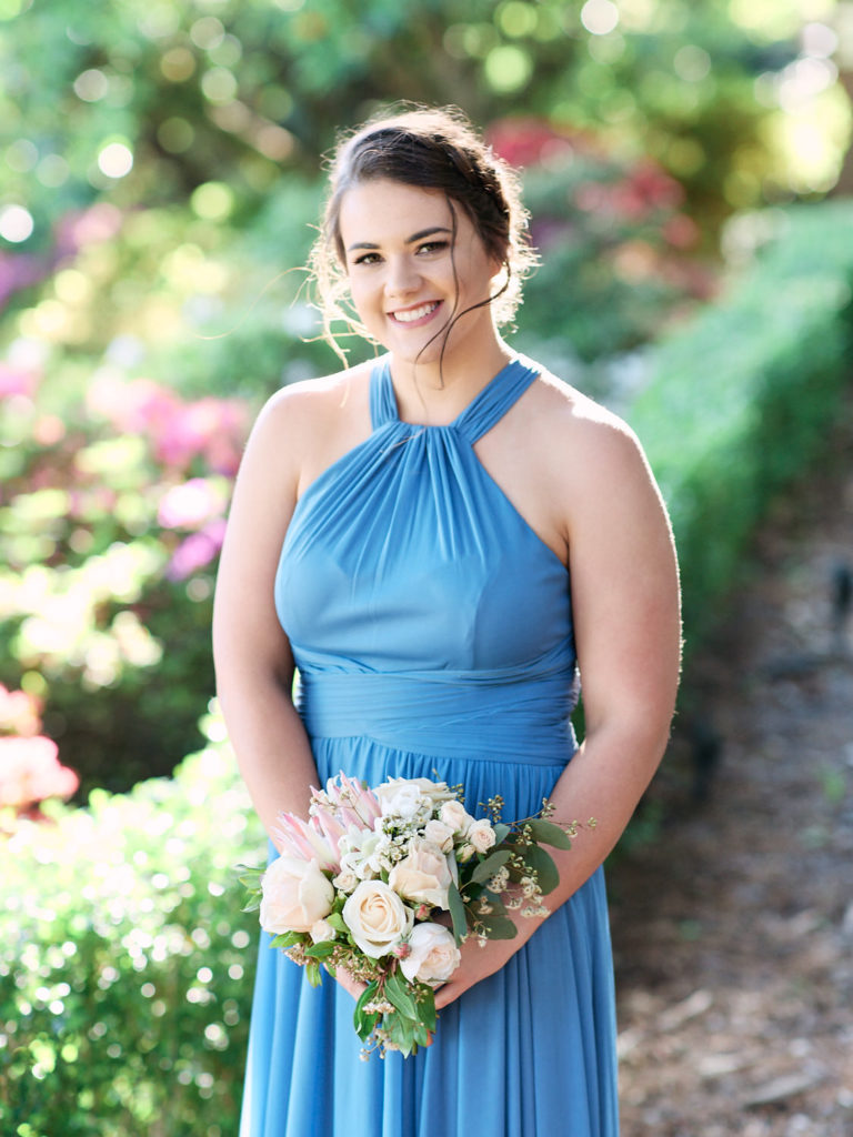 Bridesmaid wearing blue dress and holding bouquet in gardens at Echoes Boutique Hotel and Restaurant