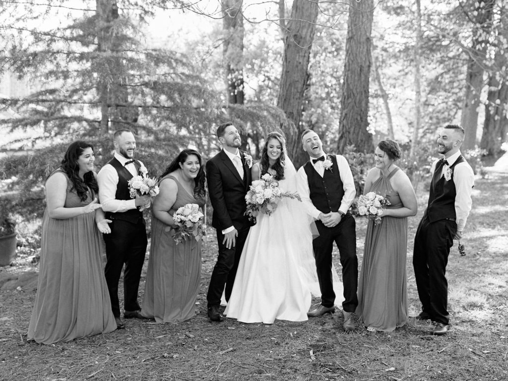 Black and white portrait of bridal party laughing in front of trees