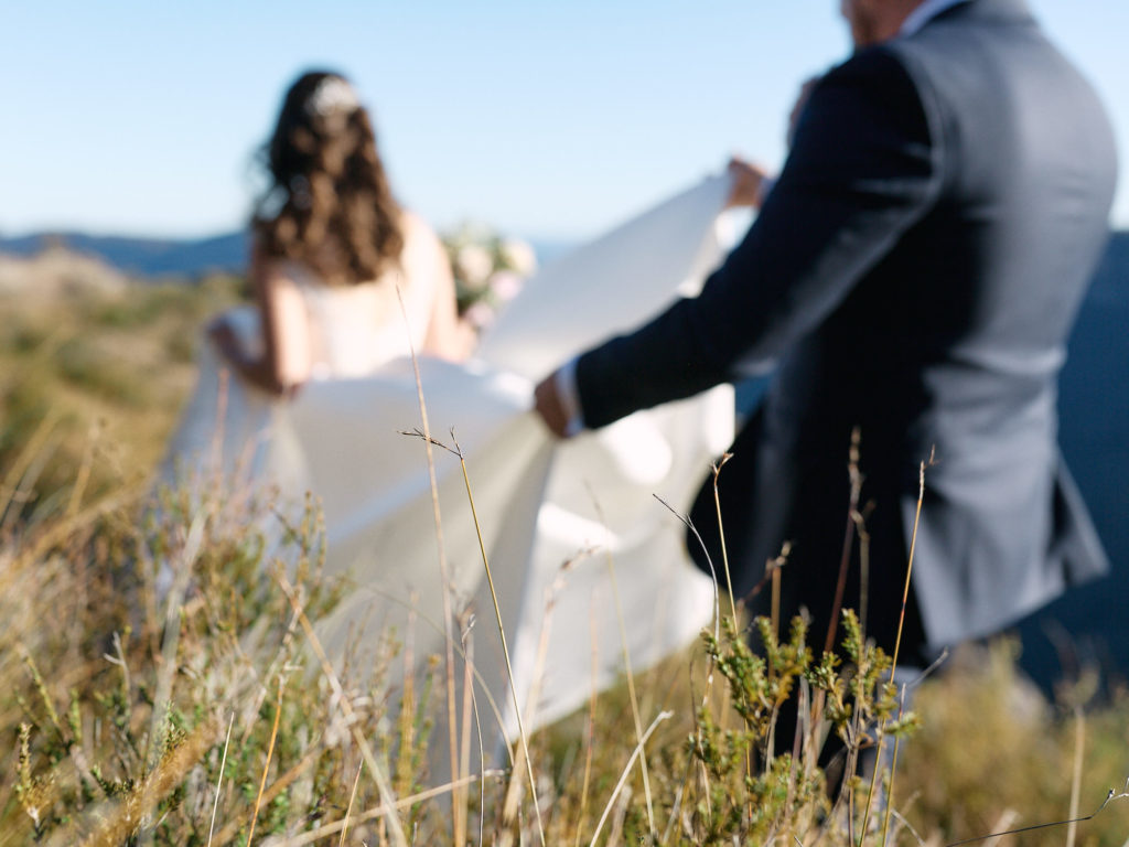 Out of focus groom holding brides dress off the ground while walking through long grass in the Blue Mountains