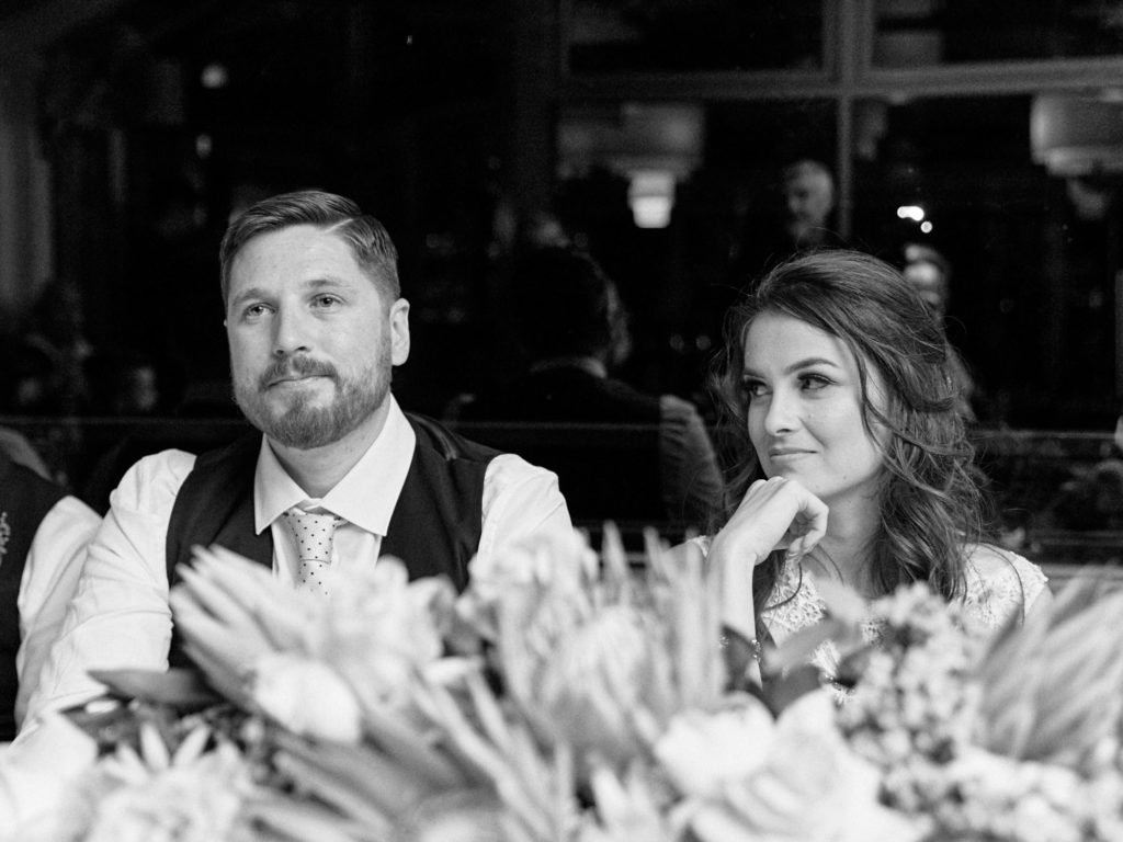 Black and white of bride watching emotional groom during speeches
